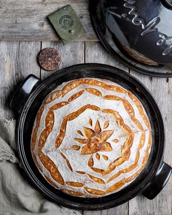  A loaf of bread is sitting on a table next to a pot made of ceramic ovenware.